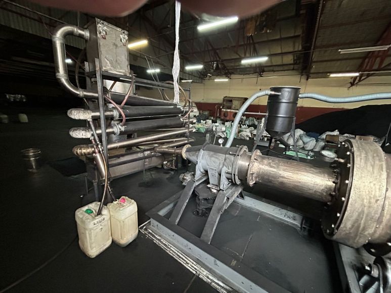 Pyrolysis distilling equipment with condensing pipework and recovered liquid product containers inside an industrial workshop.