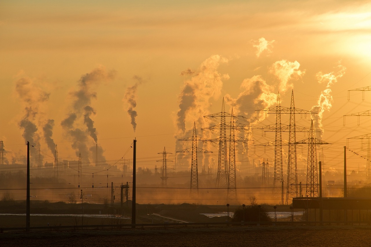 Industrial smokestacks and power transmission towers silhouetted against a hazy sunset.